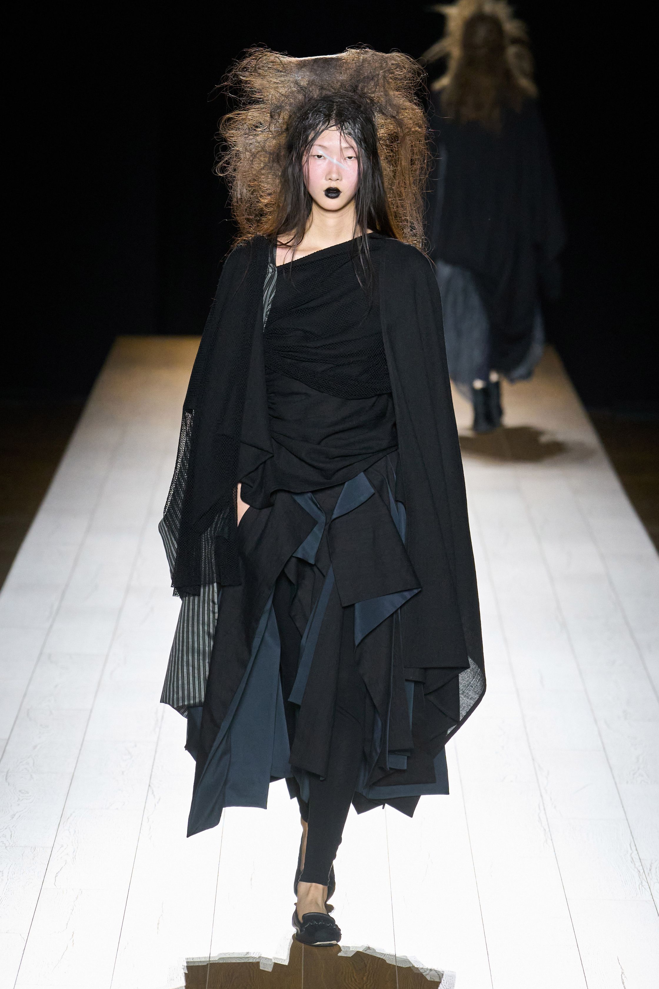 Yohji Yamamoto 本季依然延续标志性的黑色哲学：宽松层叠轮廓、和服式结构与手工拼接面料形成一种诗意而深沉的东方美学。夸张头饰与飘逸衣摆让整场秀像一场黑色戏剧，既神秘又极具艺术感-顽石频道趋势研究